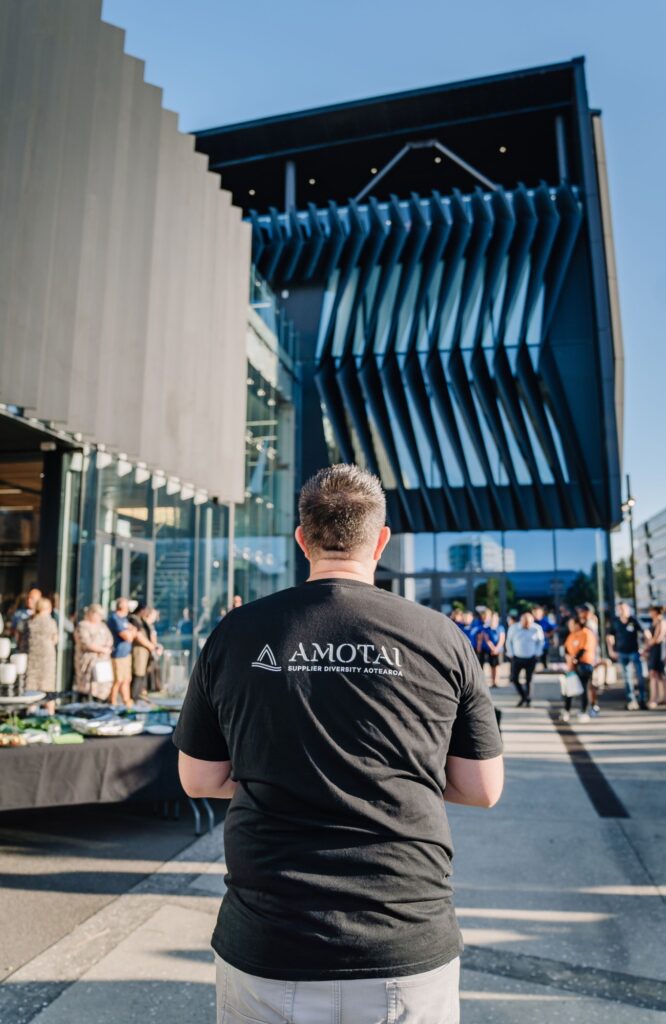 Man wearing an Amotai shirt standing outside University of Waikato, representing Amotai at the event.