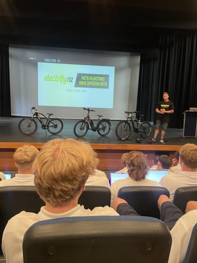 A group of students sitting in an auditorium listening to a presentation on electric bikes.