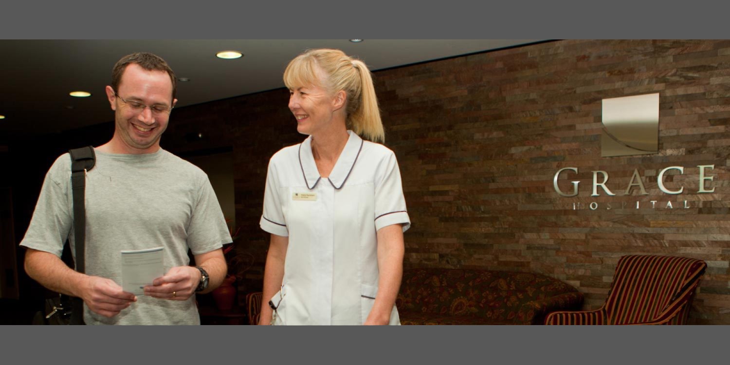 Two people walking outside the entrance of Grace Hospital with the hospital name in the background.