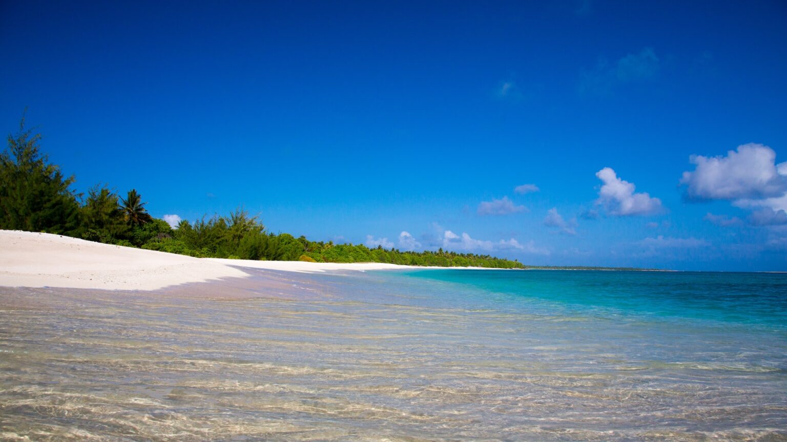 A photo of a sandy beach and blue ocean water on one of the islands in the Marshall Islands, highlighting the natural beauty of the country and its vulnerable location in the Pacific Ocean susceptible to the impacts of climate change.